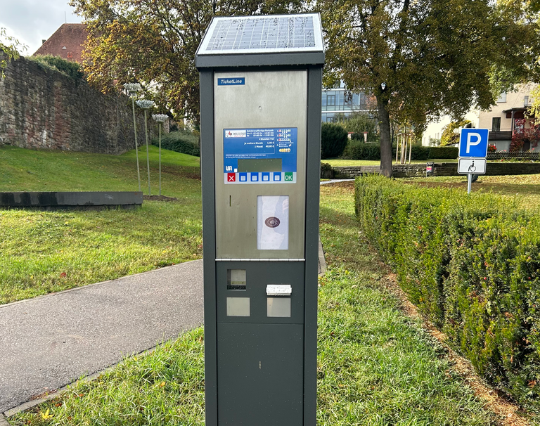 Ein Parkscheinautomat steht am Rand eines Parkplatzes.