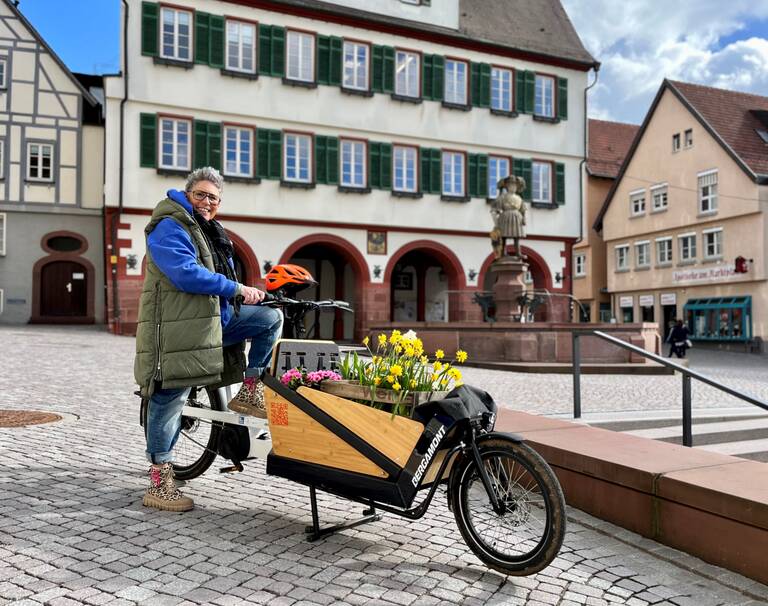 Eine Frau transportiert Blumen mit einem Lastenrad. Im Hintergrund ist das Rathaus Weil der Stadt.