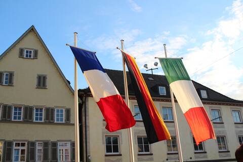 Die Flaggen von Frankreich, Deutschland und Italien wehen nebeneinander im Wind.