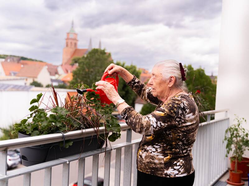 Eine Seniorin gießt Blumen. Im Hintergrund ist die Kirche St. Peter und Paul. 