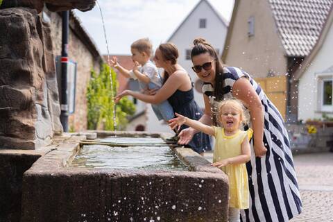 Zwei Frauen spielen mit ihren Kindern an einem Brunnen.