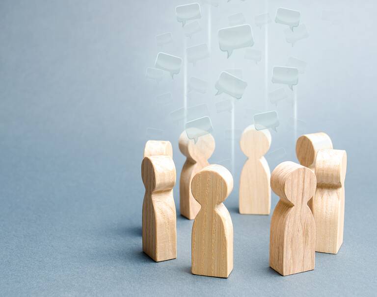 Mehrere Holzfiguren stehen in einem Kreis. Die Sprechblasen über den Figuren zeigen, dass sie miteinander kommunizieren.
