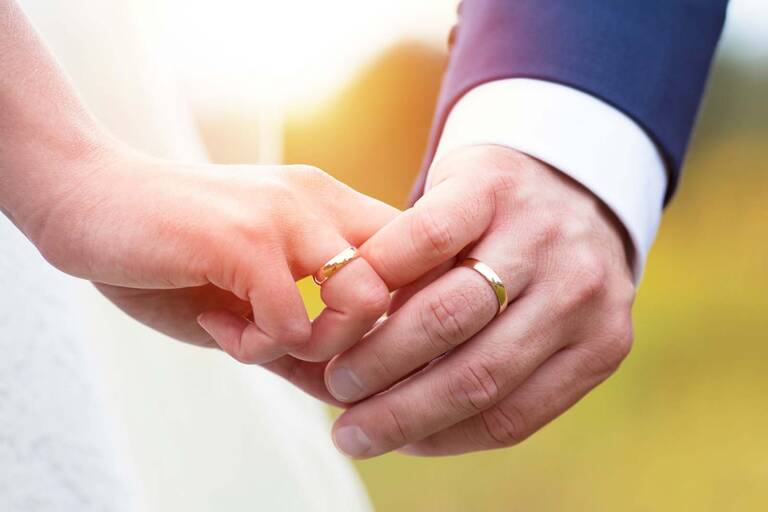 Nahaufnahme von zwei einander haltenden Händen eines Brautpaares.