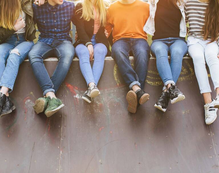 Sechs Jugendliche, die auf einer Skaterrampe sitzen und sich im Arm halten. Die Köpfe sind abgeschnitten.