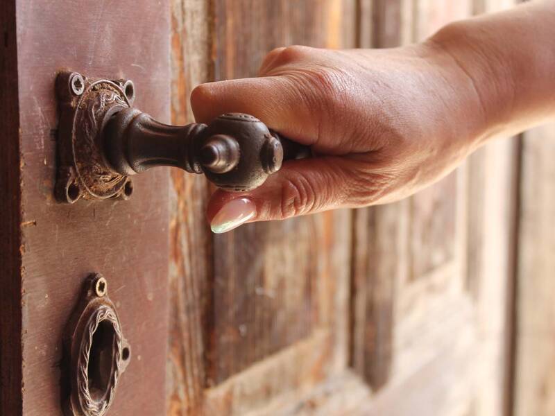 Eine Hand, die den Griff einer alten Holztür hält.